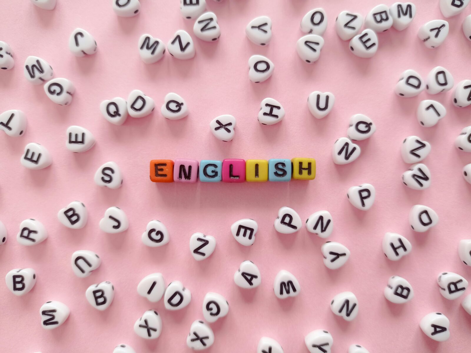 Scattered letter beads form the word 'English' on a pink background, symbolizing language learning.